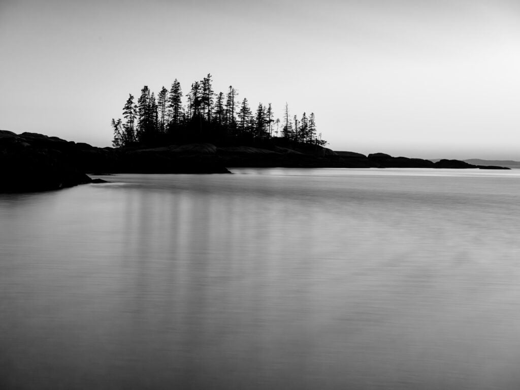 Soft Sentinels black and white long exposure photograph of spruce island silhouette at dusk over calm water, Sand Beach, Stonington, Maine, fine art landscape photography by Brad Emerson