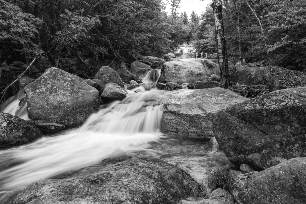 Summer Rites black and white long exposure photograph of waterfall over granite with figures at water's edge, Step Falls, Newry, Maine, fine art landscape photography by Brad Emerson