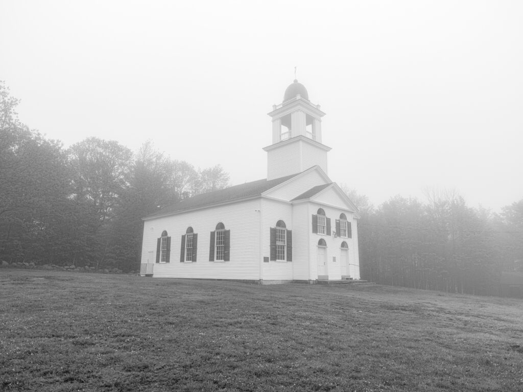 The Meeting House black and white photograph of historic white clapboard meeting house in morning fog on hilltop, Bell Hill, Otisfield, Maine, fine art landscape photography by Brad Emerson